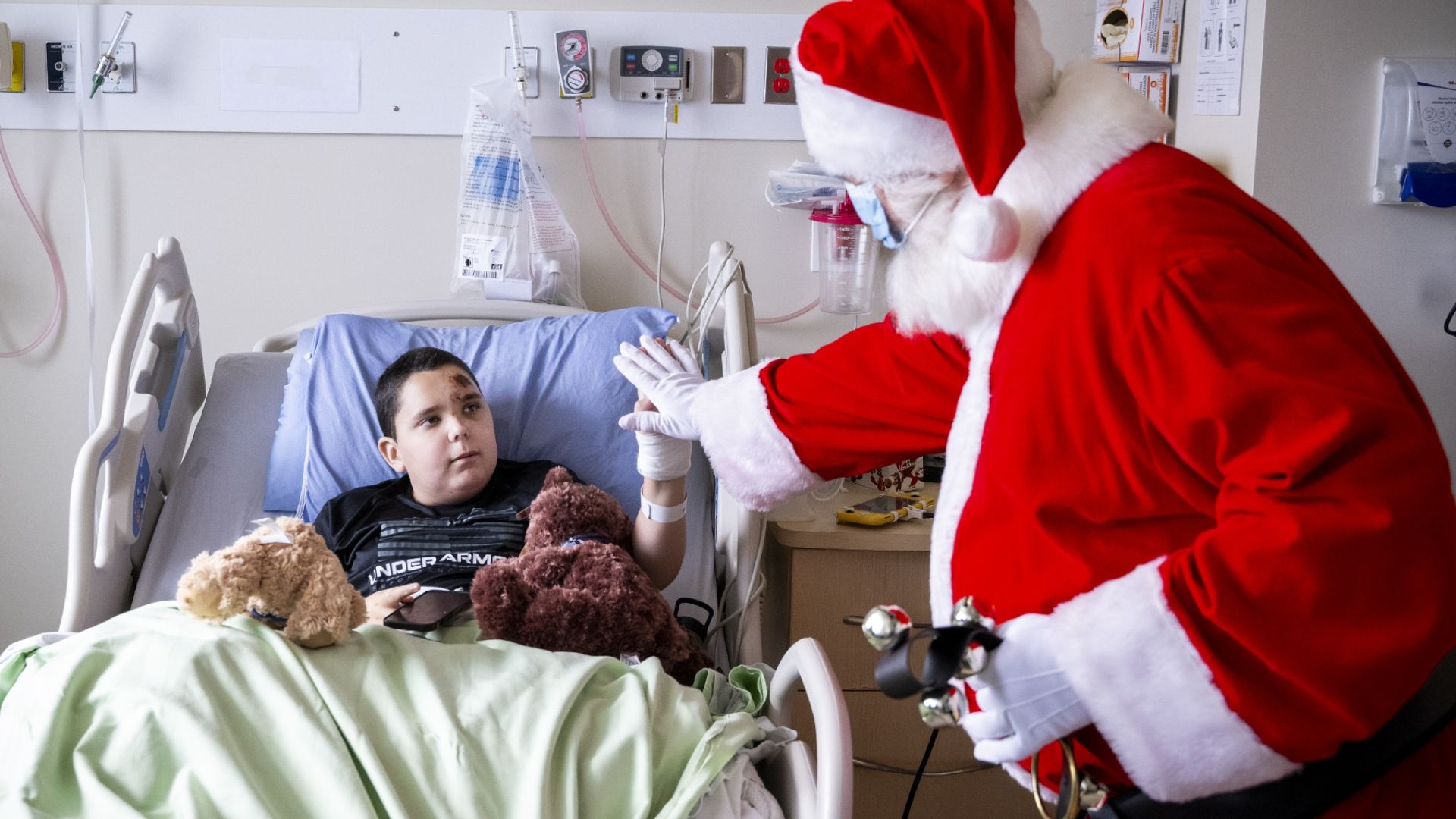 Santa high fives a young patient in a hospital bed