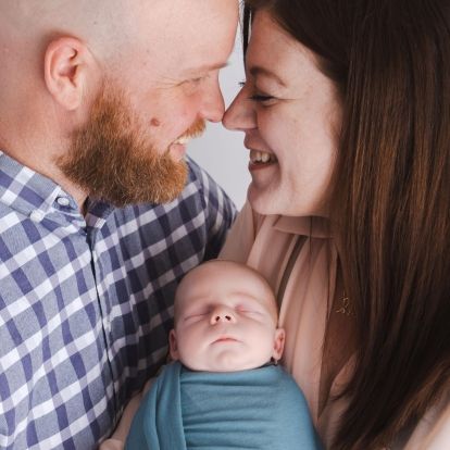 two parents holding a swaddled baby