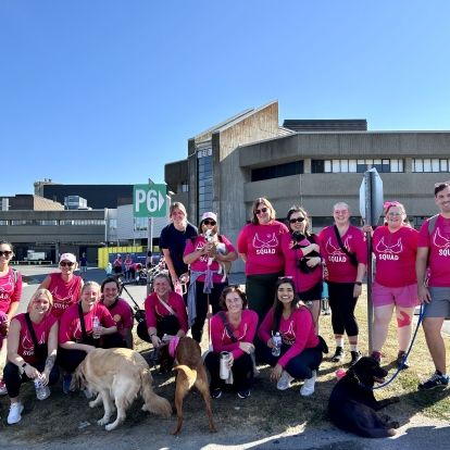 A group of KHSC employees and families wearing pink shirts in a field.