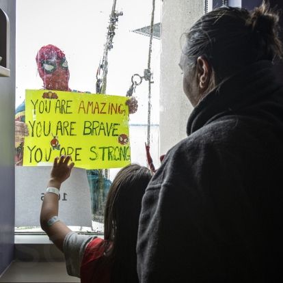 spiderman holds a sign up to a child in the hospital