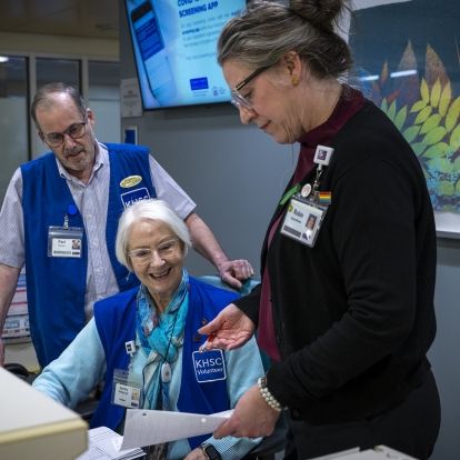 Dorothy Messenger is pictured inside the waiting room at KHSC’s Intensive Care Unit. She has short white hair and wears black framed glasses. She’s wearing a long sleeved, blue sweater with a blue vest with the words KHSC volunteer written on it.
