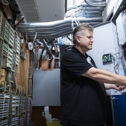 People of KHSC - Andrew Schick Andrew Schick is photographed working on equipment at the Kingston General Hospital site. He has short, salt and pepper hair, blue eyes and is wearing a black polo shirt.