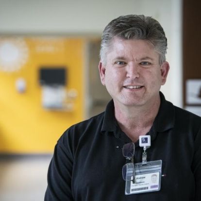 Andrew Schick is photographed standing in a hallway at the Kingston General Hospital site. He has short, salt and pepper hair, blue eyes and is wearing a black polo shirt.