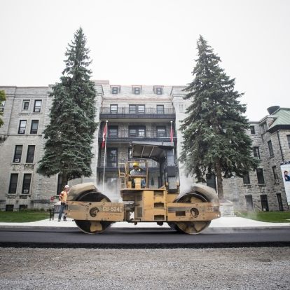 A roller flattens hot, fresh asphalt on Stuart Street in front of the Watkins wing entrance.