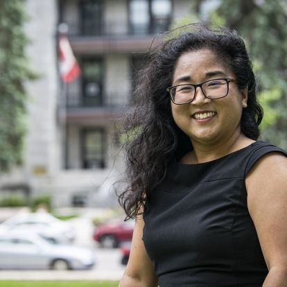 Dr. Yuka Asai has shoulder length, dark and wavy hair. She wears glasses and is wearing a black, capped sleeve top.