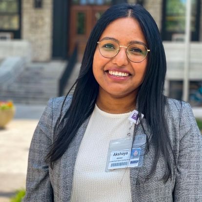 A mid shot image of Akshaya Arun who has shoulder length black hair and brown eyes, and is wearing a grey blazer and white top.