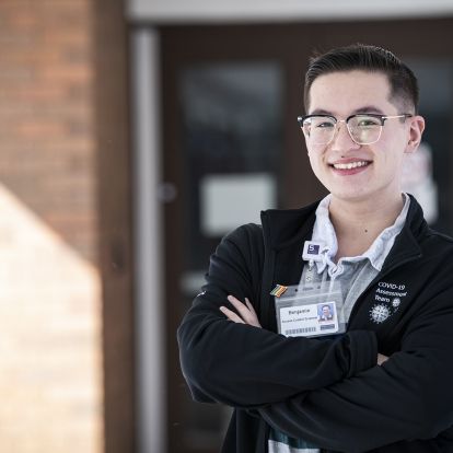 Benjamin Ma is pictured outside the COVID-19 Assessment Centre at the Beechgrove Complex. He has short dark hair and wears glasses. He's wearing a black jacket on top of a grey, collared shirt.