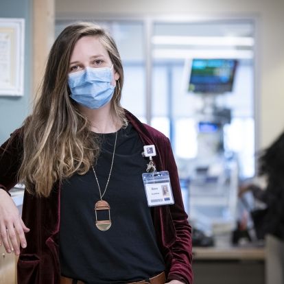 Bianca Sabatini is pictured leaning on the care desk at the Intensive Care Unit (ICU) at the KGH site. She has blue eyes and medium brown, wavy hair that goes down past her shoulders. She’s wearing a black top with a burgundy blazer on top.