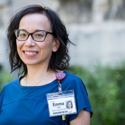 A mid shot image of Emma Hum who has chin length dark, wavy hair, brown eyes and is wearing a blue top.