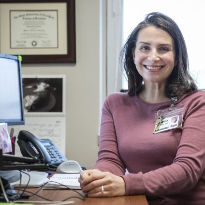 Joanna Elliott is pictured sitting at her desk at the Hotel Dieu Hospital site. She has shoulder length, dark brown hair and is wearing a mauve blouse.