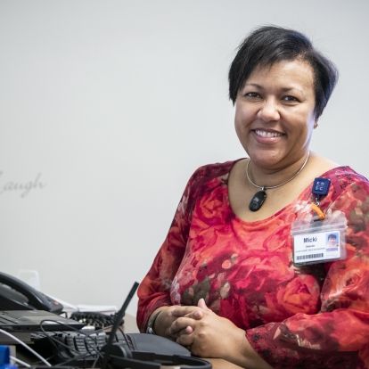 Micki Mulima is pictured sitting at her desk at the KGH site. She has short, dark hair and is wearing a red, patterned top.