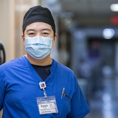 Ralph Yeung is pictured in a hallway at the KGH site. He's wearing blue scrubs, a mask and black scrub hat.