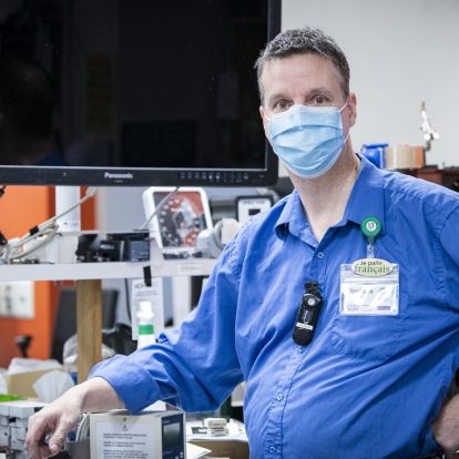 Stéphane Bois has short, salt and pepper hair. He’s wearing a long-sleeve blue shirt and mask. He’s picture inside the Clinical Engineering department at the Kingston General Hospital site.