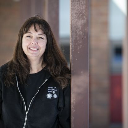 Tricia Anderson is pictured outside the COVID-19 Assessment Centre at the Beechgrove Complex. She has shoulder length, dark brown hair with bangs, and is wearing a black jacket on top of a black shirt.