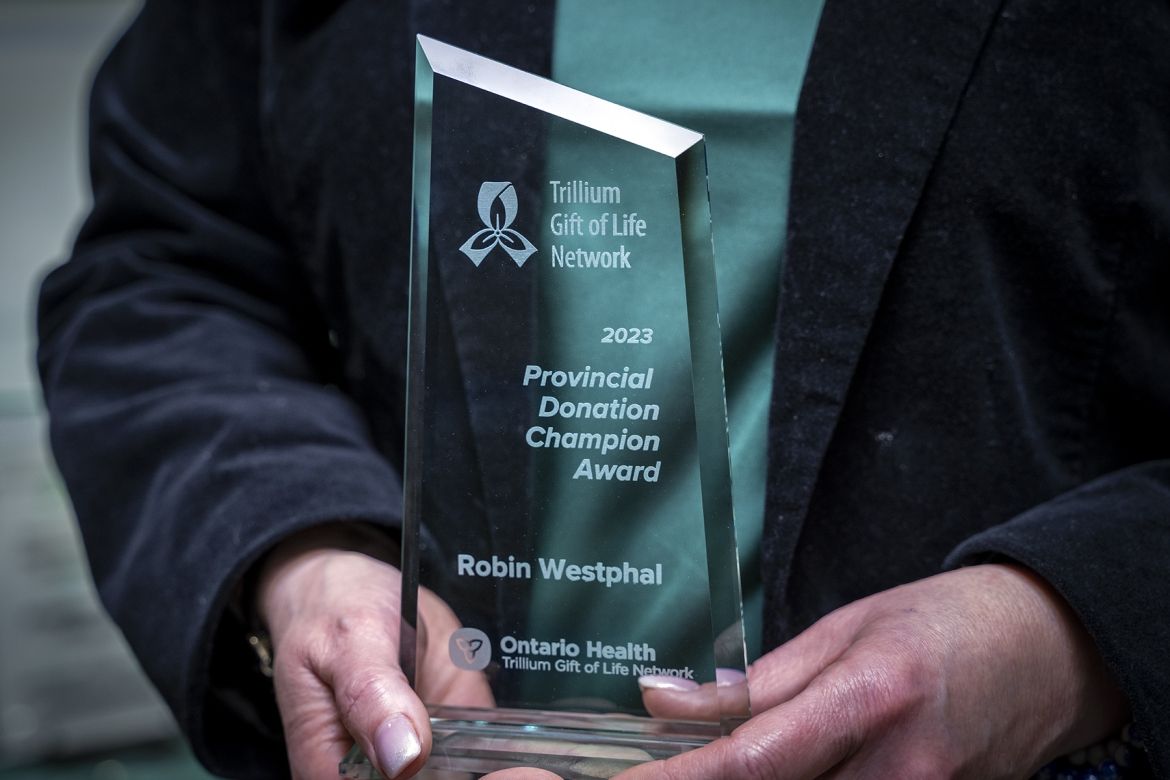 PoKHSC: Robin Westphal This is a close up shot of the 2023 Provincial Donor Champion Award, being held in Robin Westphal’s hands. The award is made of glass. Etched on it is 2023 Provincial Donor Champion Award, Ontario Health Trillium Gift of Life Network and Robin Westphal.