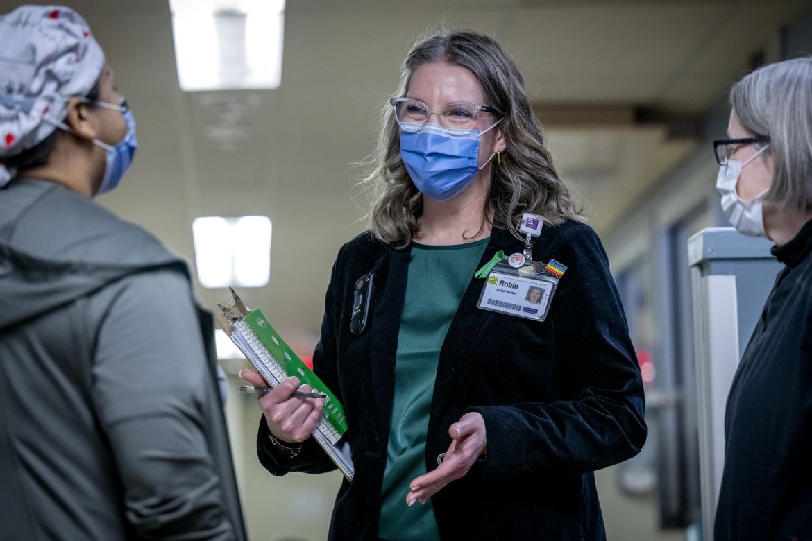 PoKHSC: Robin Westphal Robin Westphal is pictured standing in the middle of two colleagues in the Intensive Care Unit. Robin has dirty blonde hair with grey streaks, blue eyes and wears glasses. She’s wearing a green blouse with a black blazer on top. All three individuals are wearing masks.