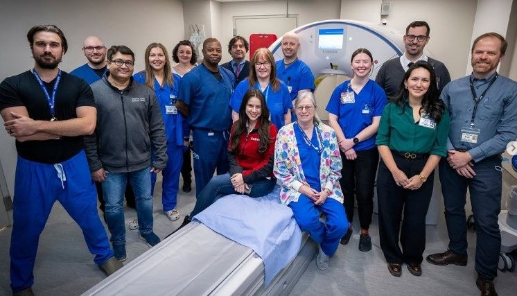 Staff members gather in front of imaging machine.