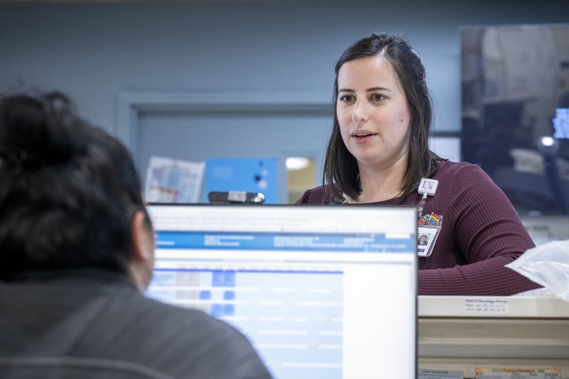 Paola standing by a counter, speaking to a staff member on a computer