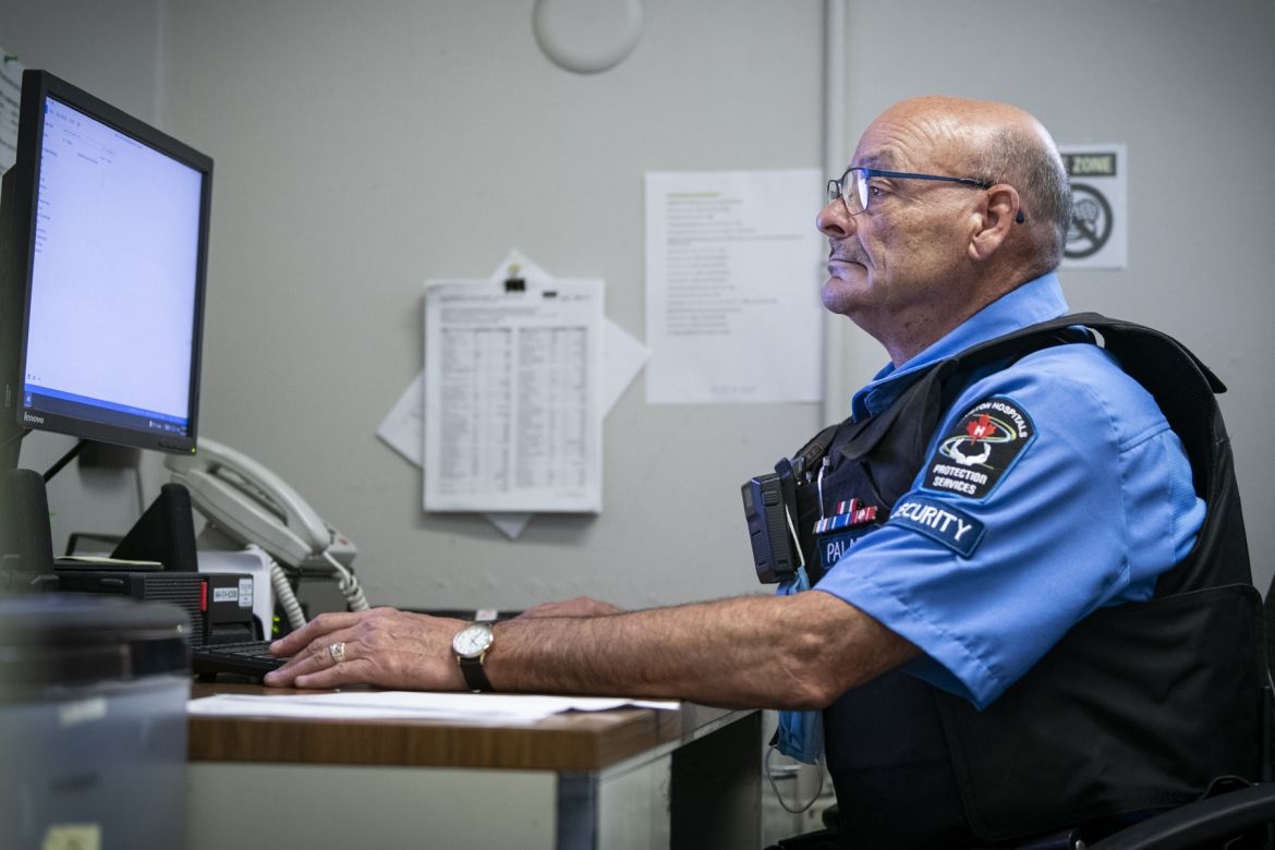 People of KHSC: Mario Lelievre 2 Mario Lelievre is pictured sitting at his desk looking at a monitor at Hotel Dieu Hospital. He has brown eyes, wears blue glasses and is bald. He’s wearing his Paladin Security uniform, which includes a blue collared, button down shirt, protective vest, radio, and ID badge.