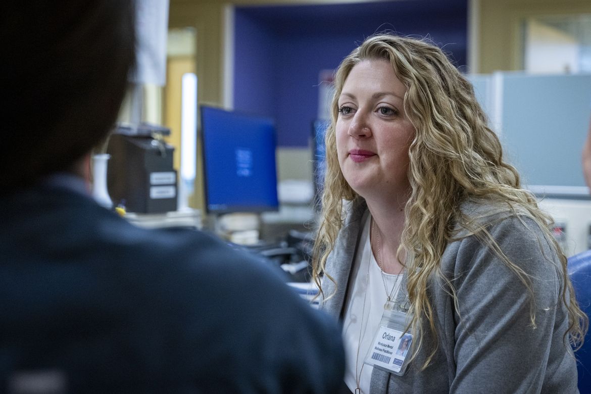 People of KHSC - Orlana Bourgoin Orlana Bourgoin is sitting on a chair at a care desk in an inpatient unit at the Kingston General Hospital site, looking at a colleague. She has long, wavy, blonde hair, blue eyes and is wearing a grey blazer with a white blouse underneath.