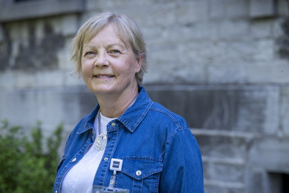 People of KHSC - Patti Cox Patti Cox is pictured smiling directly at the camera while standing outside at Kingston General Hospital. She has blue eyes and light blonde hair styled in a pixie cut. She’s wearing a blue denim blouse on top of a white t-shirt.