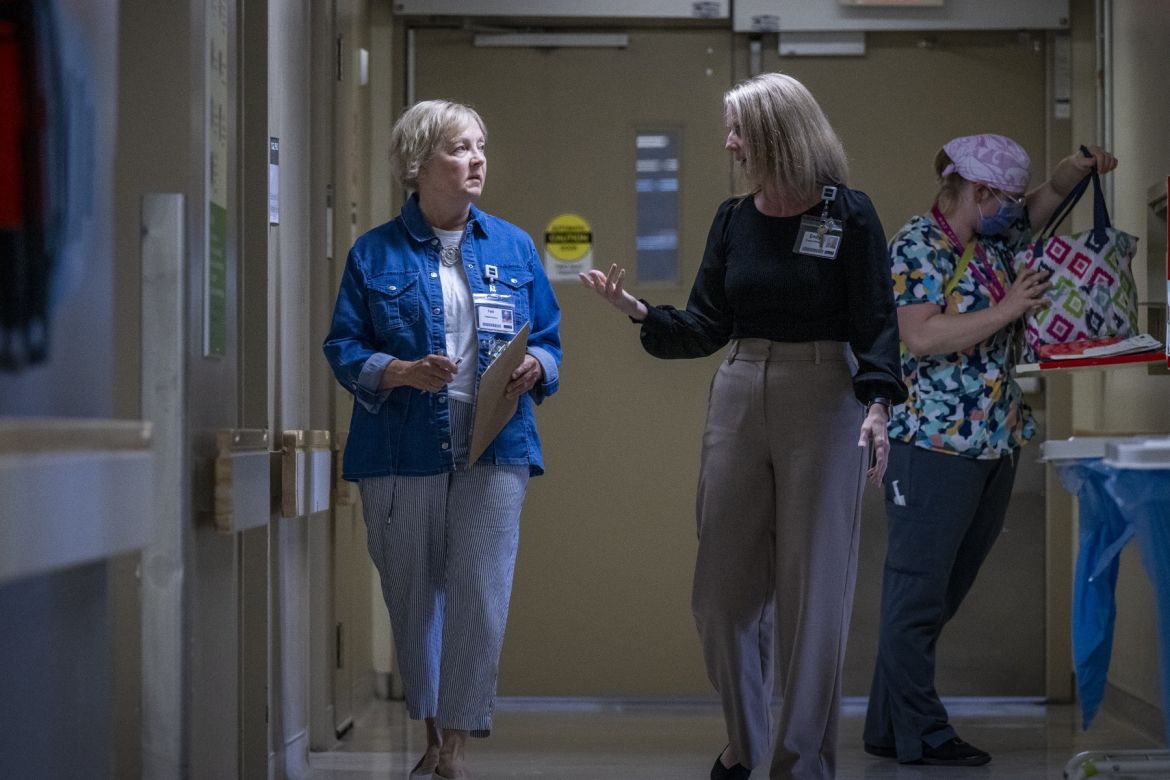 People of KHSC - Patti Cox Patti Cox is pictured walking and talking with a member of patient care team down a hallway on an in-patient unit. Cox has blue eyes and light blonde hair styled in a pixie cut. She’s wearing a blue denim blouse on top of a white t-shirt, and is holding a clipboard and pen. The care team member has should length blonde hair, and is wearing a black blouse with light brown dress pants.