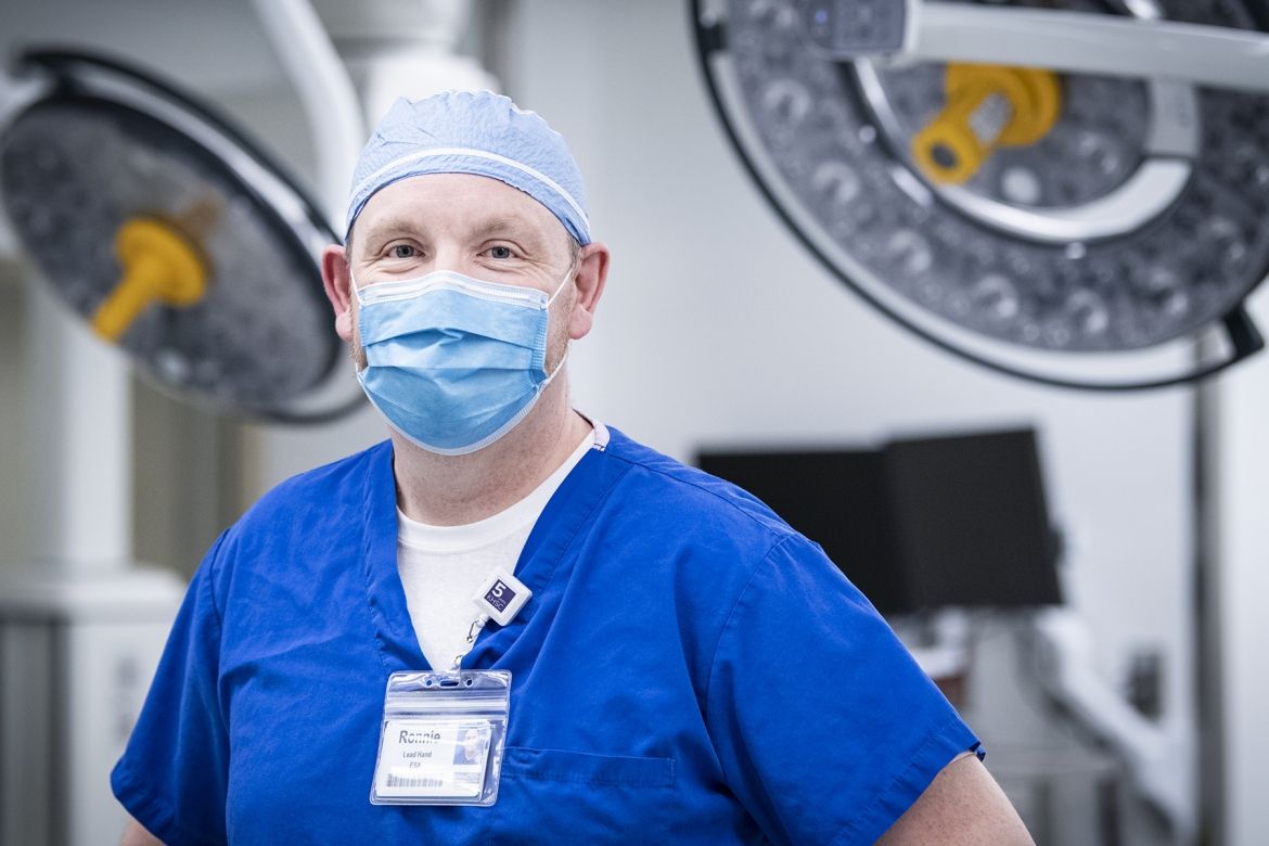 Ronnie Lott is pictured standing inside one of the operating rooms at the KGH site. He has blue eyes and is wearing blue scrubs, a scrub hat and mask.