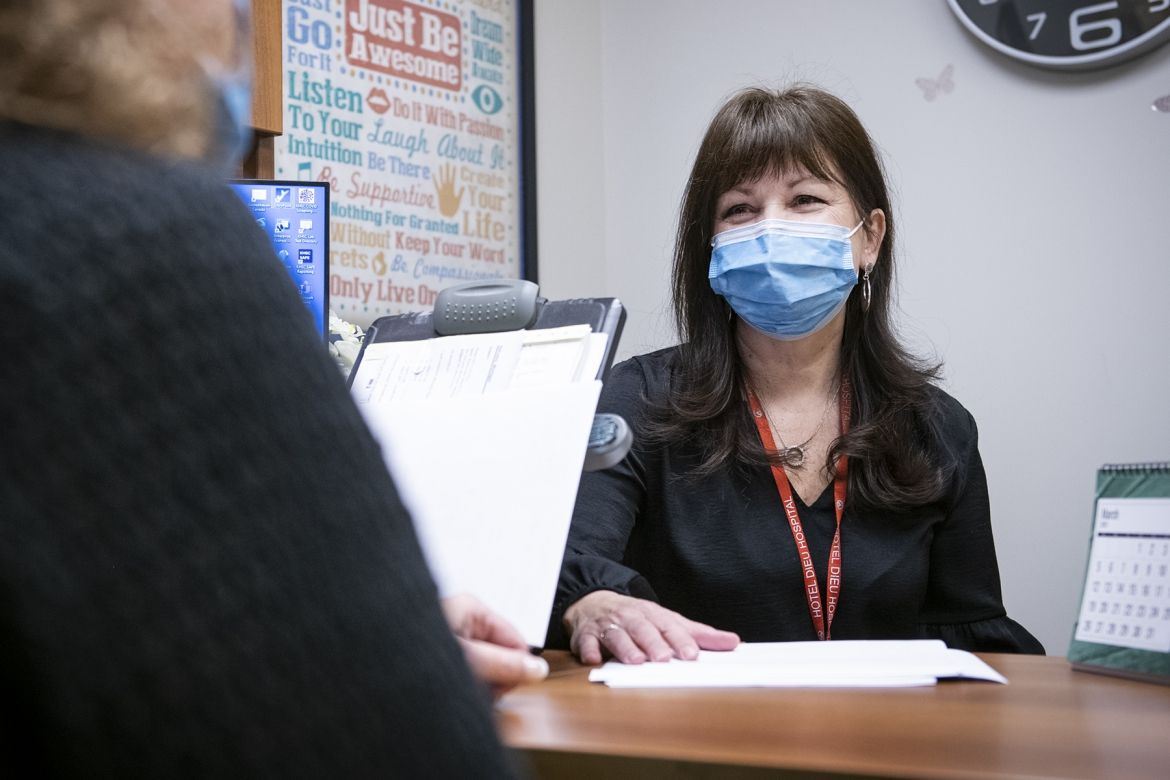 Sandra Mahoney is pictured sitting at her desk in Johnson 5 at the HDH site. She has dark brown, shoulder length hair and brown eyes. She’s wearing a black blouse and mask.