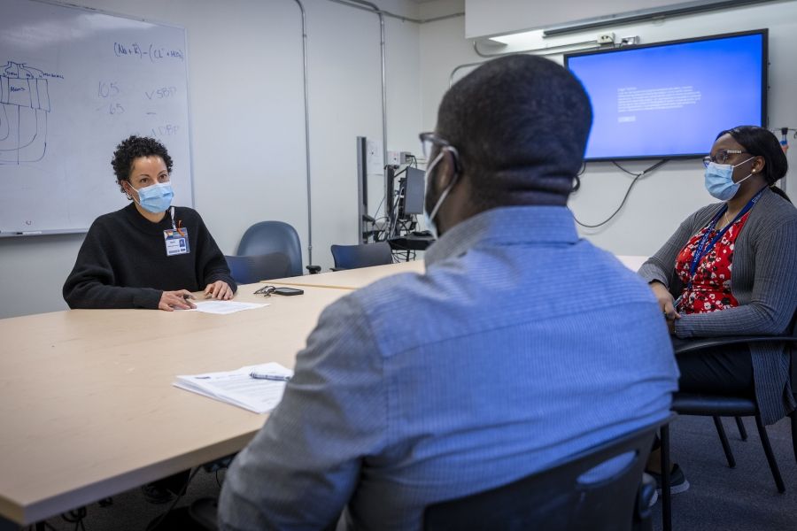Black Staff Community Group 2 Members of the Black Staff Community Group are seated around a boardroom table as they meet. There are two Black women and one Black man. All have papers in front of them.