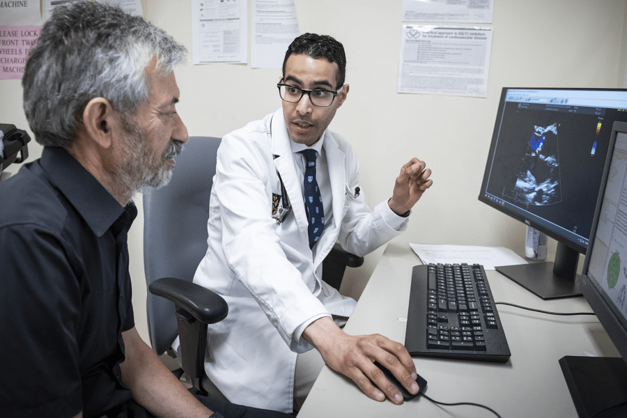 Dr. Almufleh is pictured sitting in front of a computer talking to a colleague at the Heart Function Clinic.