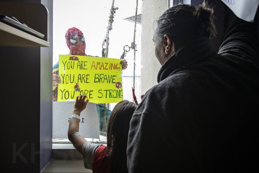 spiderman holds a sign up to a child in the hospital