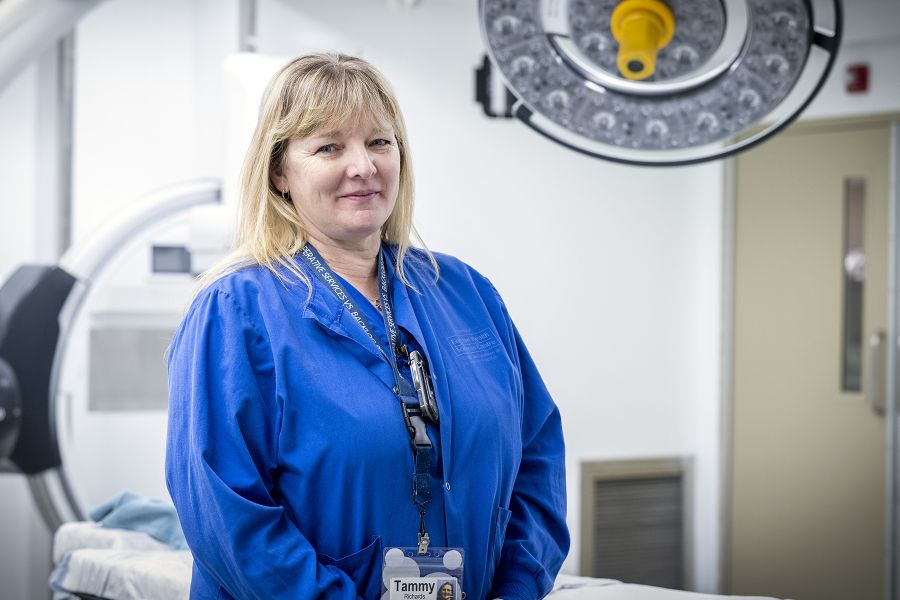 Tammy Richards is standing in the OR smiling directly at the camera for her headshot. She has long blonde hair, blue eyes and is wearing blue scrubs.
