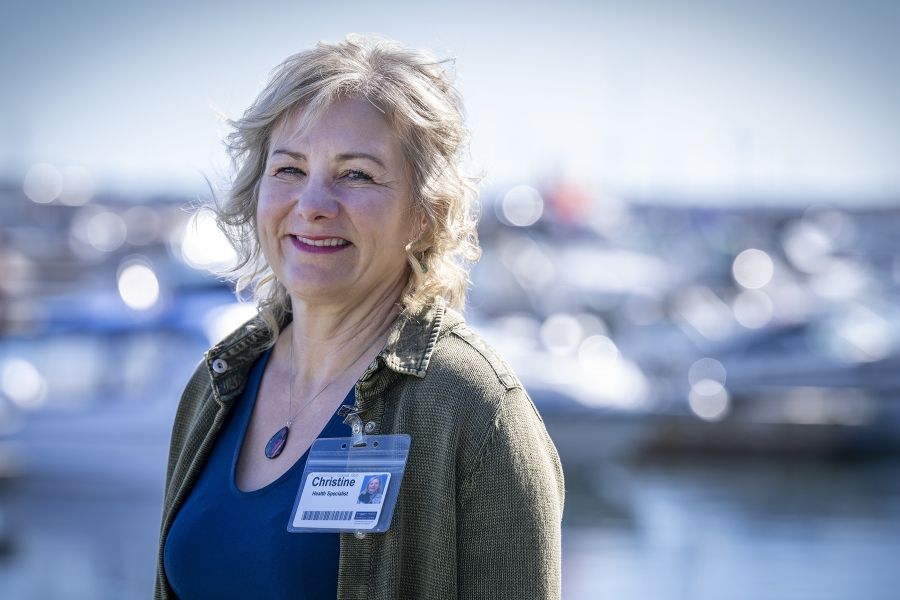 Christine Hennigar is photographed standing outside of Geaganano Residence. She’s smiling directly into the camera. She has light blonde, wavy hair, blue eyes and is wearing a navy blue top with an army green jacket.