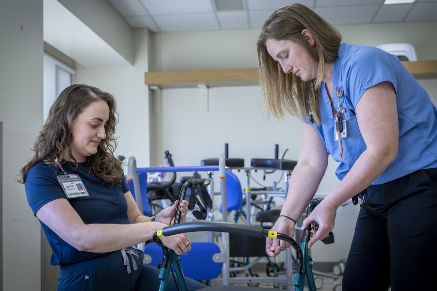 PeopleOfKHSC_Justine_White_11 Justine White and physiotherapy assistant Danielle Knapton are putting together a walker, a mobility aid device. White has shoulder length, medium brown, wavy hair and brown eyes. She’s wearing a navy blue shirt with her KHSC ID badge. Knapton has straight medium brown hair and blue eyes. She’s wearing light blue scrubs with her KHSC ID badge.