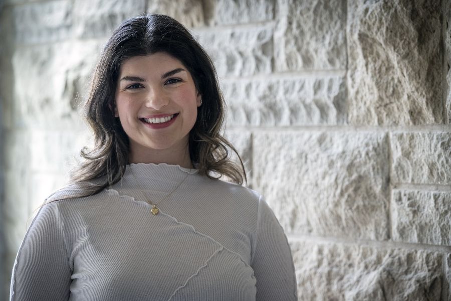 PeopleOfKHSC_Andreea_Bocicariu_10 Andreea Bocicariu is standing against a wall and smiling directly into the camera. She has brown wavy hair, brown eyes and is wearing a white blouse with a gold heart necklace.