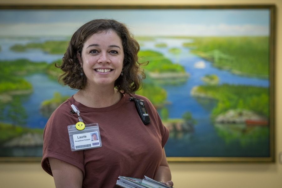 PeopleofKHSC_Laurie_Hill_12 Laurie Hill is photographed in a hallway. She’s looking directly at the camera and smiling. She has short brown wavy hair and is wearing a dusty rose blouse and black pants.