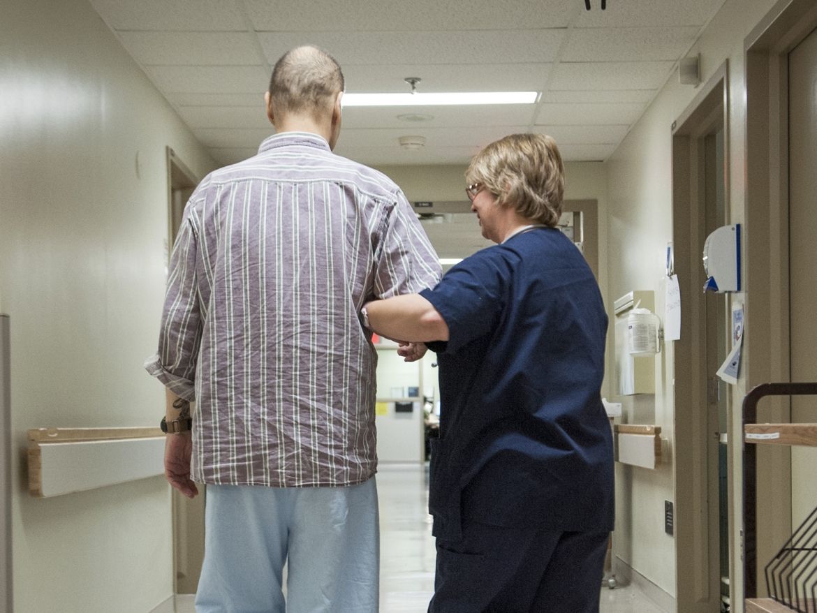 A nurse helping a patient wlak down the hallway