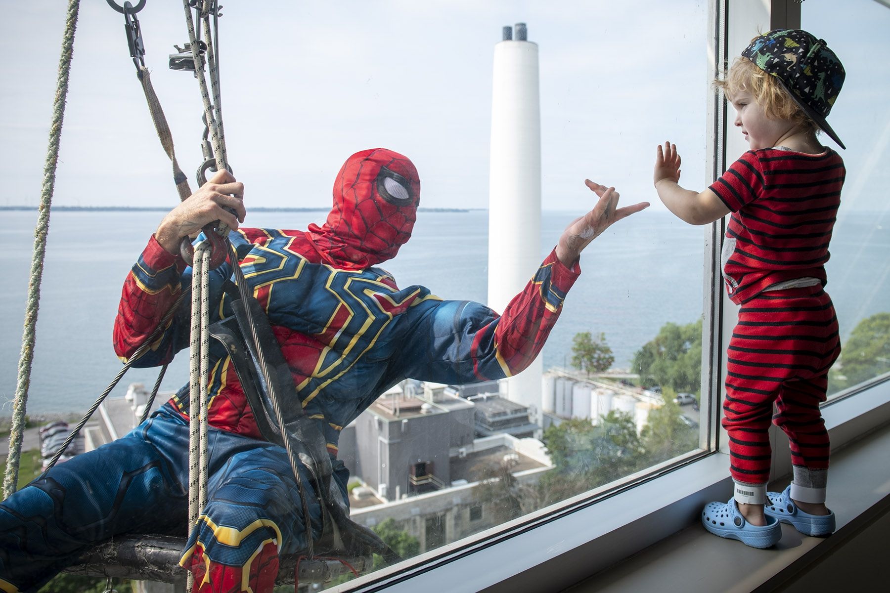 Spiderman shares a moment with child on pediatrics unit of KHSC. Image of Spiderman window washer with child at window