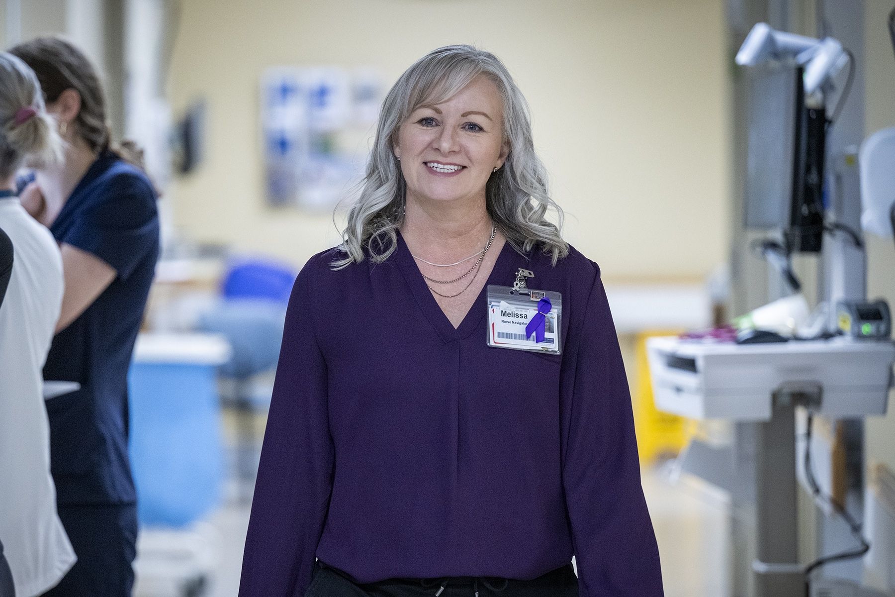 PeopleOfKHSC_Melissa_Meisner_5 Melissa Meisner is walking down a hallway and smiling. Meisner has blue eyes, shoulder length, silver hair and is wearing a bright purple blouse.