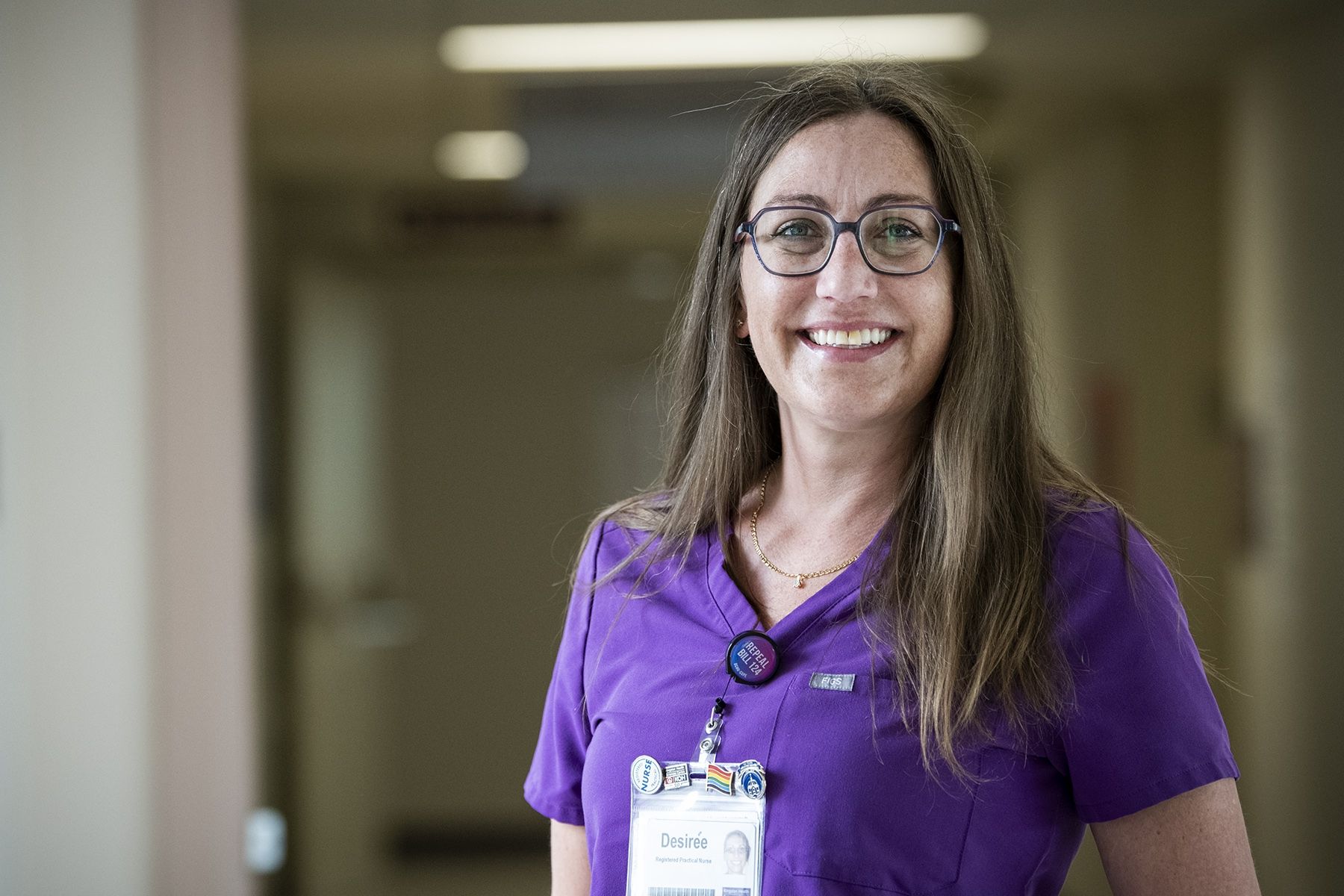 Desirée vandenTillaart is a RPN with KHSC's Kingston Bariatric Centre of Excellence. Desirée vandenTillaart is photographed standing in a hallway at the Kingston Bariatric Centre of Excellence, located at the Hotel Dieu Hospital site. She has straight, medium brown hair that goes past her shoulders. She has blue eyes, wears glasses and is wearing purple scrubs.