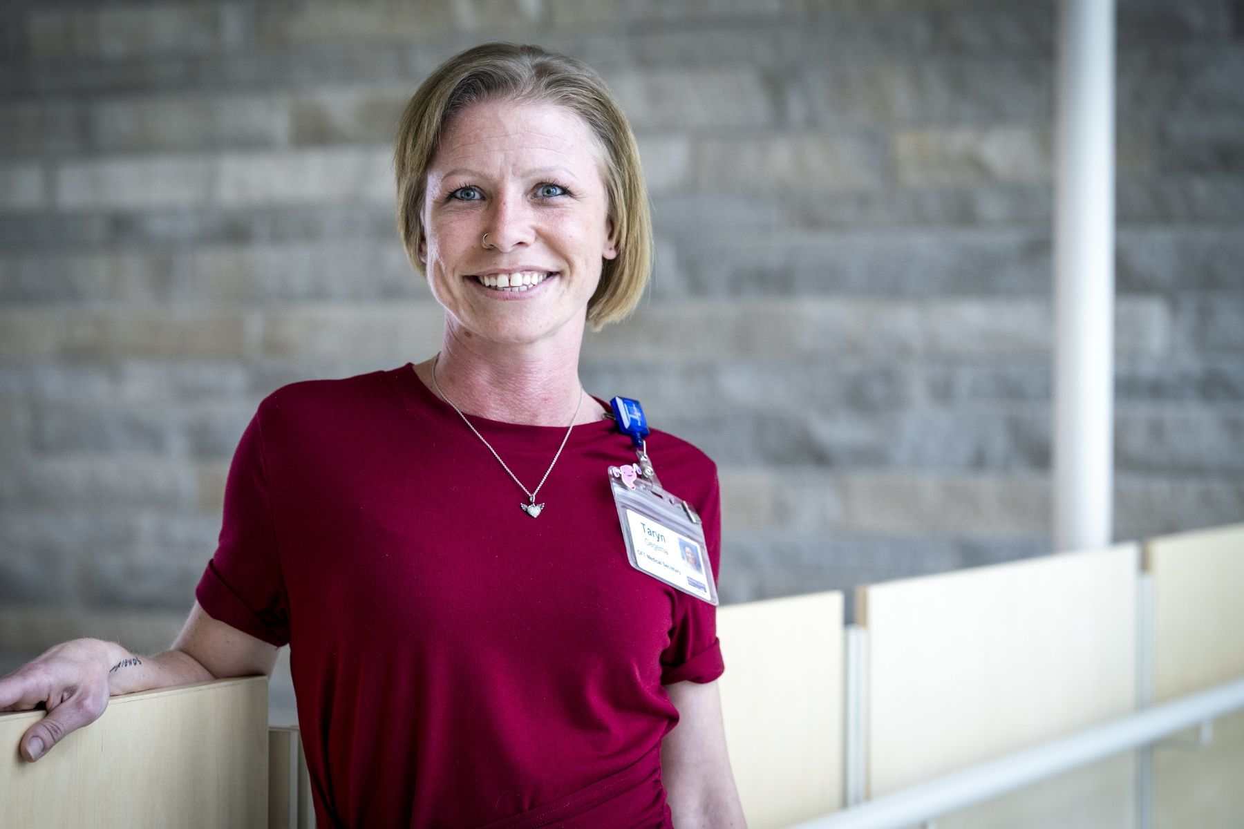 People of KHSC - Taryn Oegema Taryn Oegema is pictured standing and leaning against a bannister in a hallway at Kingston General Hospital. She has short blonde hair, blue eyes and has a big smile on her face. She’s wearing a dark red blouse.