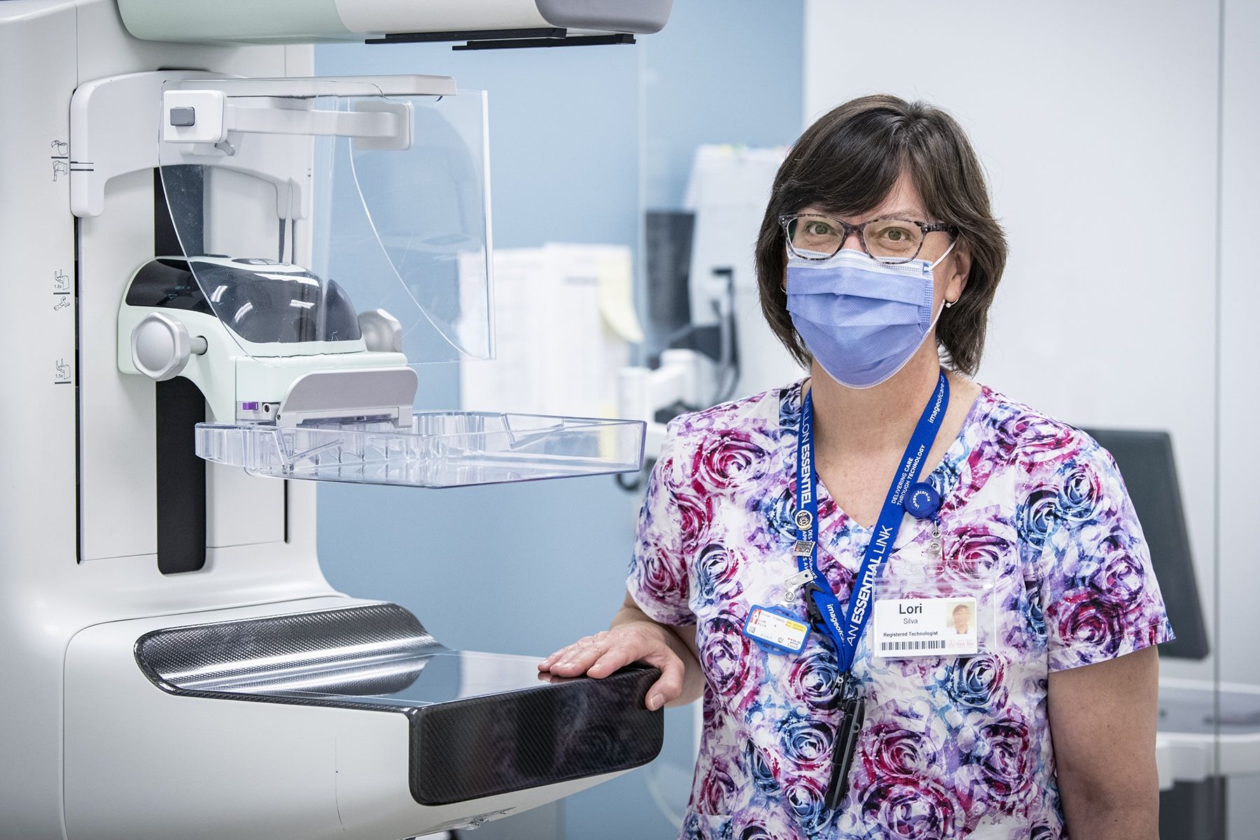 Lori Silva has short, dark hair and has glasses. She's pictured standing next to a piece of equipment at Breast Imaging Kingston.