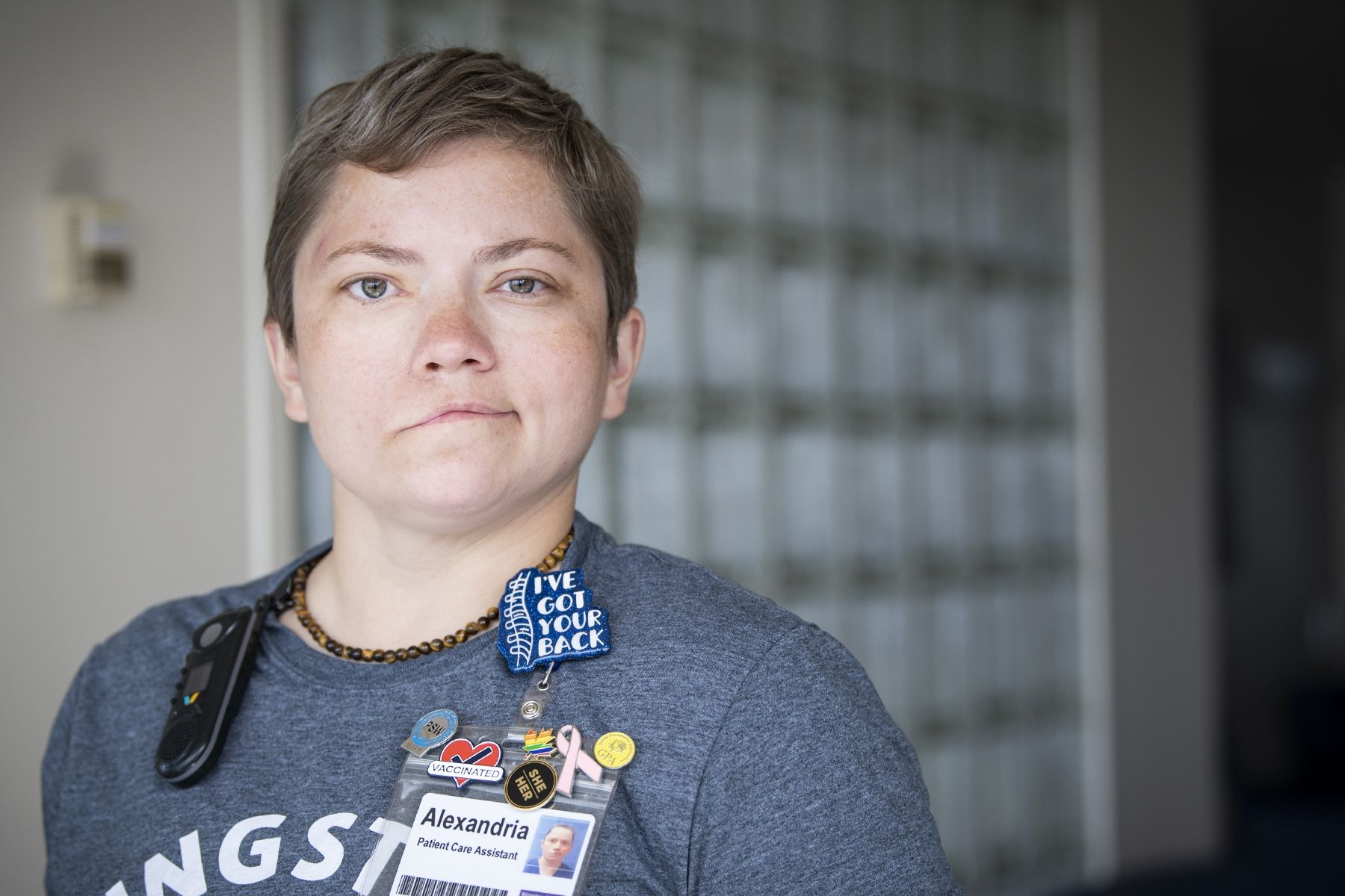Alex Paudyn has short, light brown hair and greenish/brown eyes. She’s wearing a dark blue t-shirt with a pin above our KHSC ID badge that says “I’ve got your back”. She’s pictured in a hallway at Kingston General Hospital.