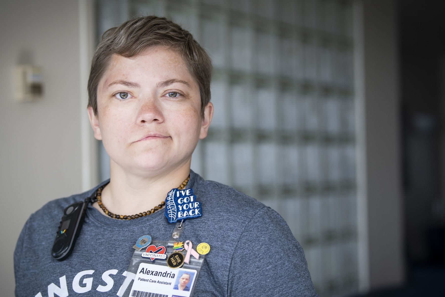 Alex Paudyn has short, light brown hair and greenish/brown eyes. She’s wearing a dark blue t-shirt with a pin above our KHSC ID badge that says “I’ve got your back”. She’s pictured in a hallway at Kingston General Hospital.  