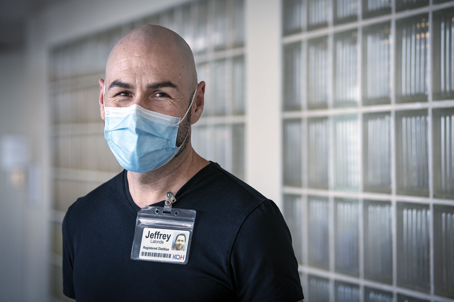 Jeffrey Lalonde is pictured in a hallway at the KGH site. He has dark brown eyes and is bald. He’s wearing a navy blue, V-neck top. 